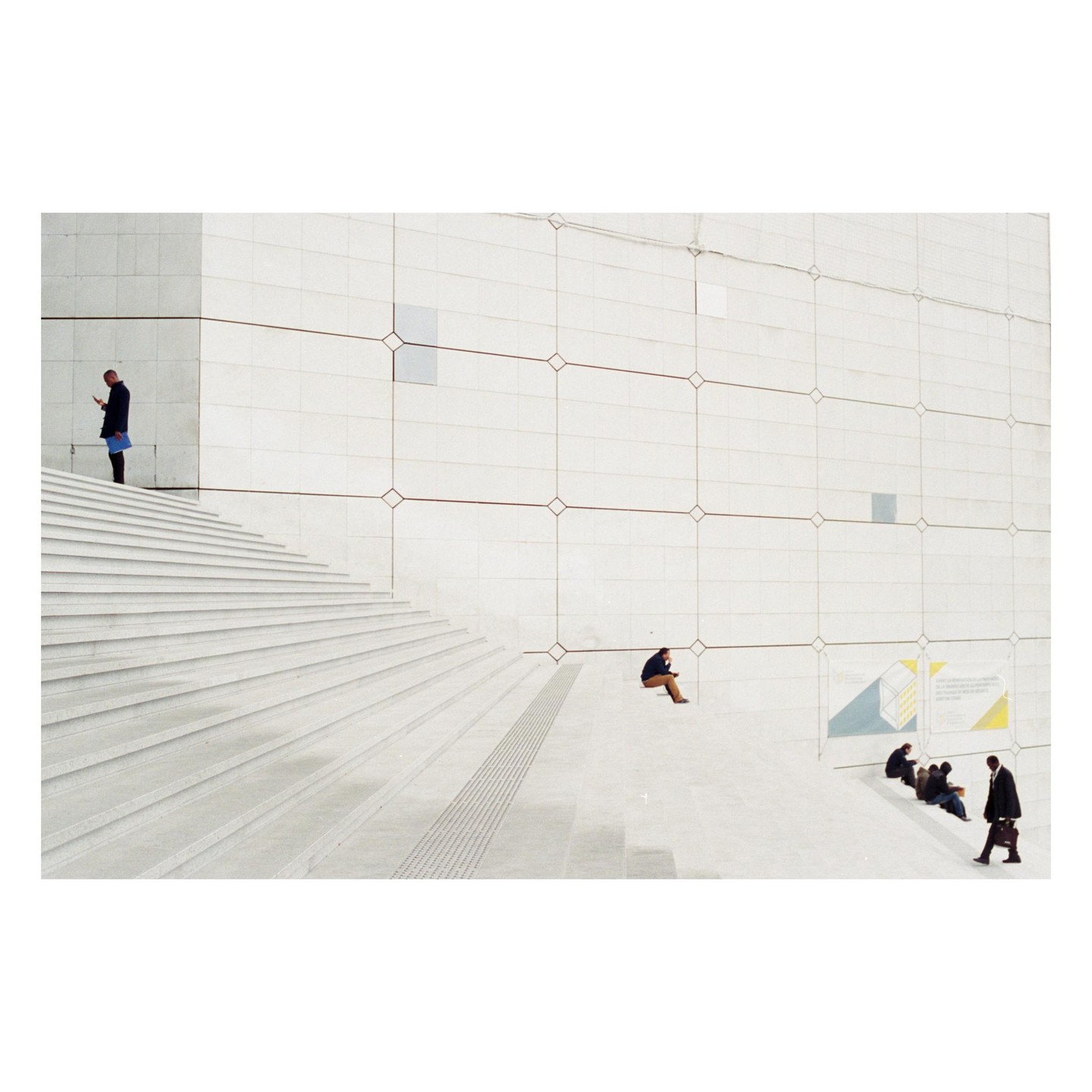 Several men are on a large white staircase and wall with geometric patterns.