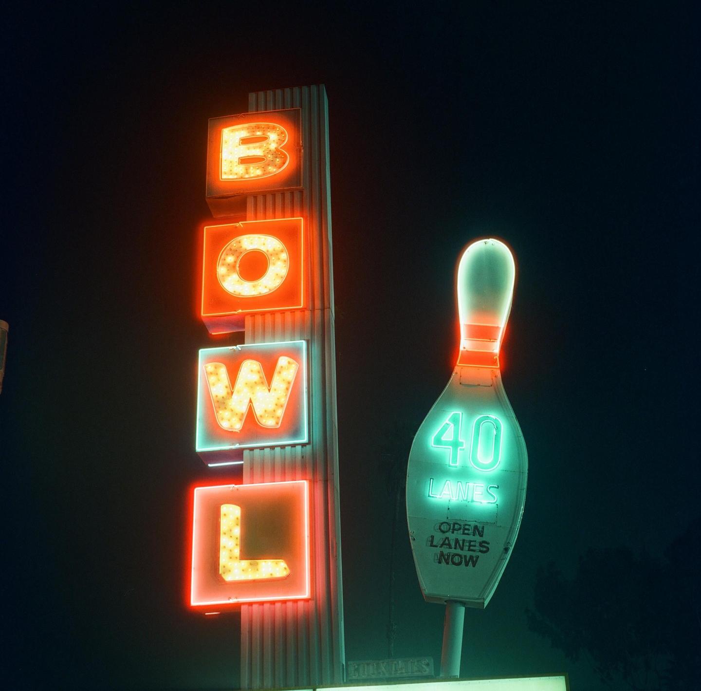 A neon sign for a bowling alley glows brightly against the dark night sky.