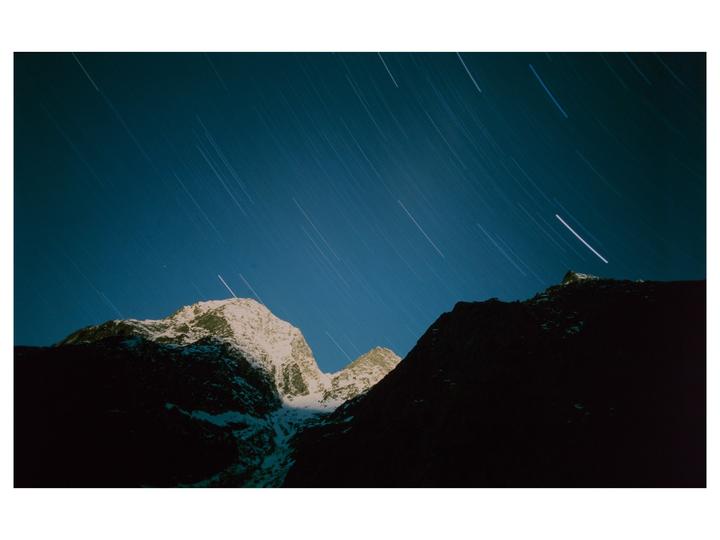 A snow-capped mountain peak is illuminated under a night sky filled with star trails.