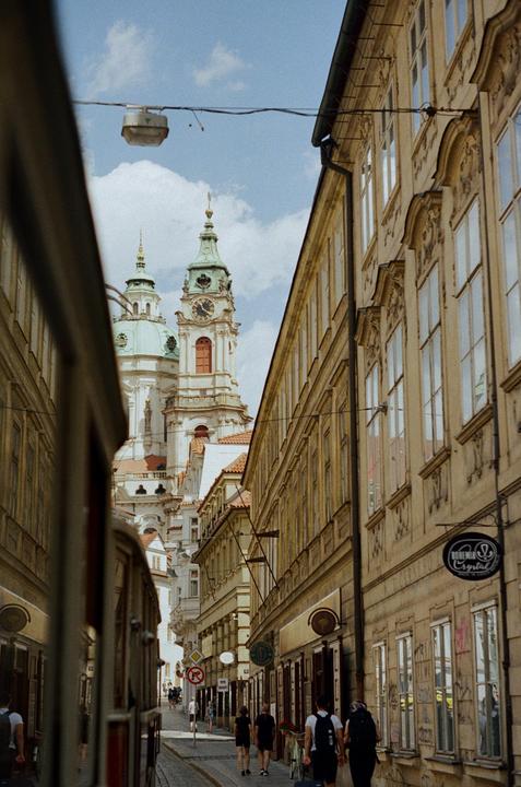 A narrow street in Prague leads to the St. Nicholas Church with its prominent clock tower.