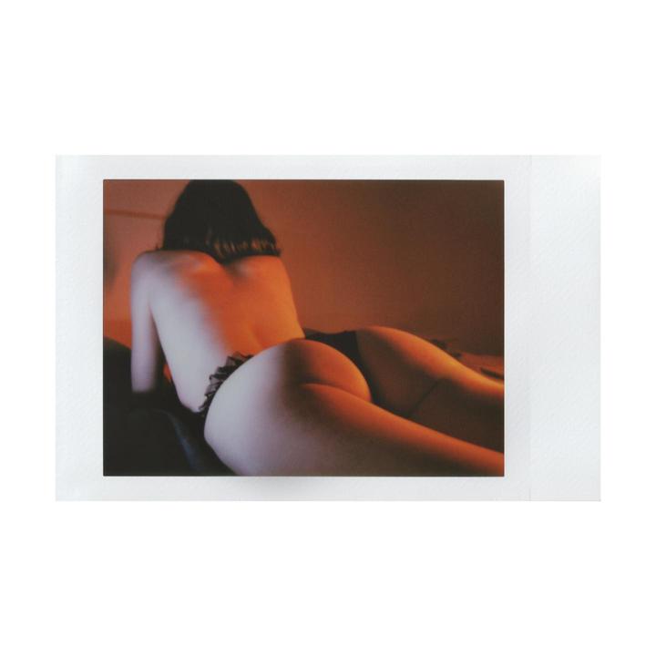 A woman is lying on her stomach, facing away from the camera, with her back and buttocks visible.