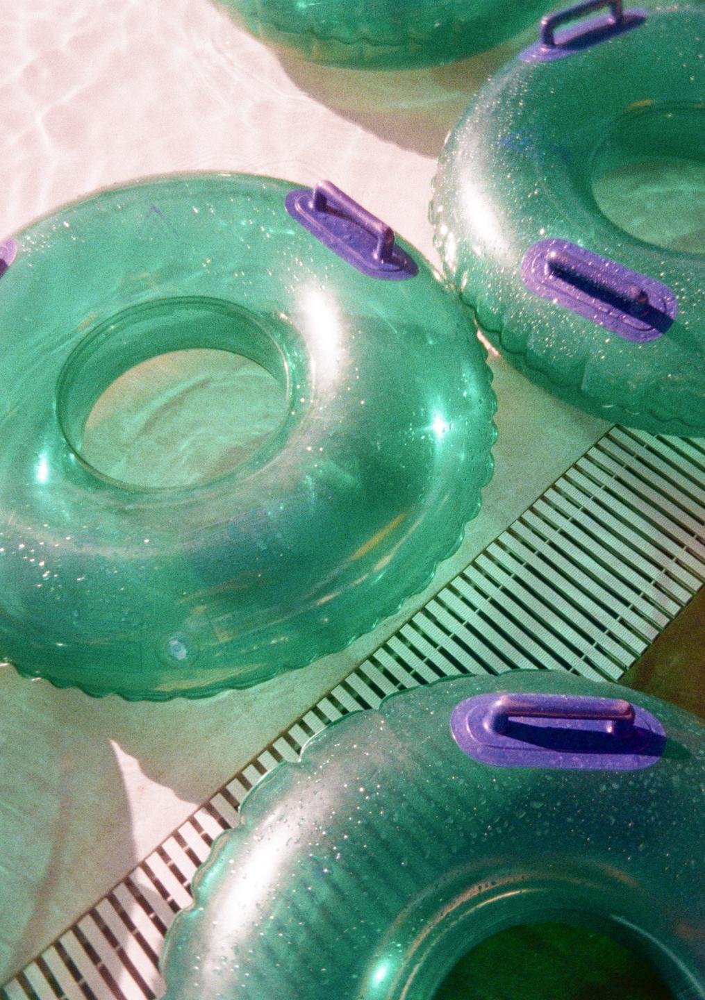 Three green inflatable tubes with purple handles float in a swimming pool next to a drain.