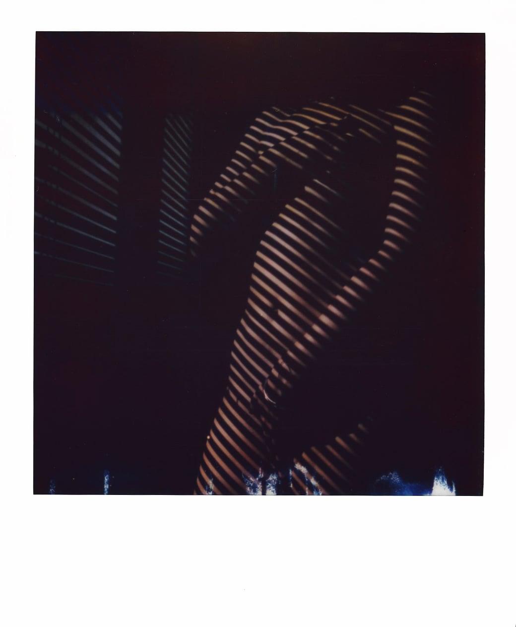 A person's torso is illuminated by striped shadows from window blinds.