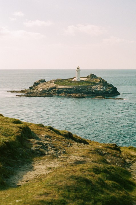 A white lighthouse stands on a rocky island covered with green grass, surrounded by the sea.