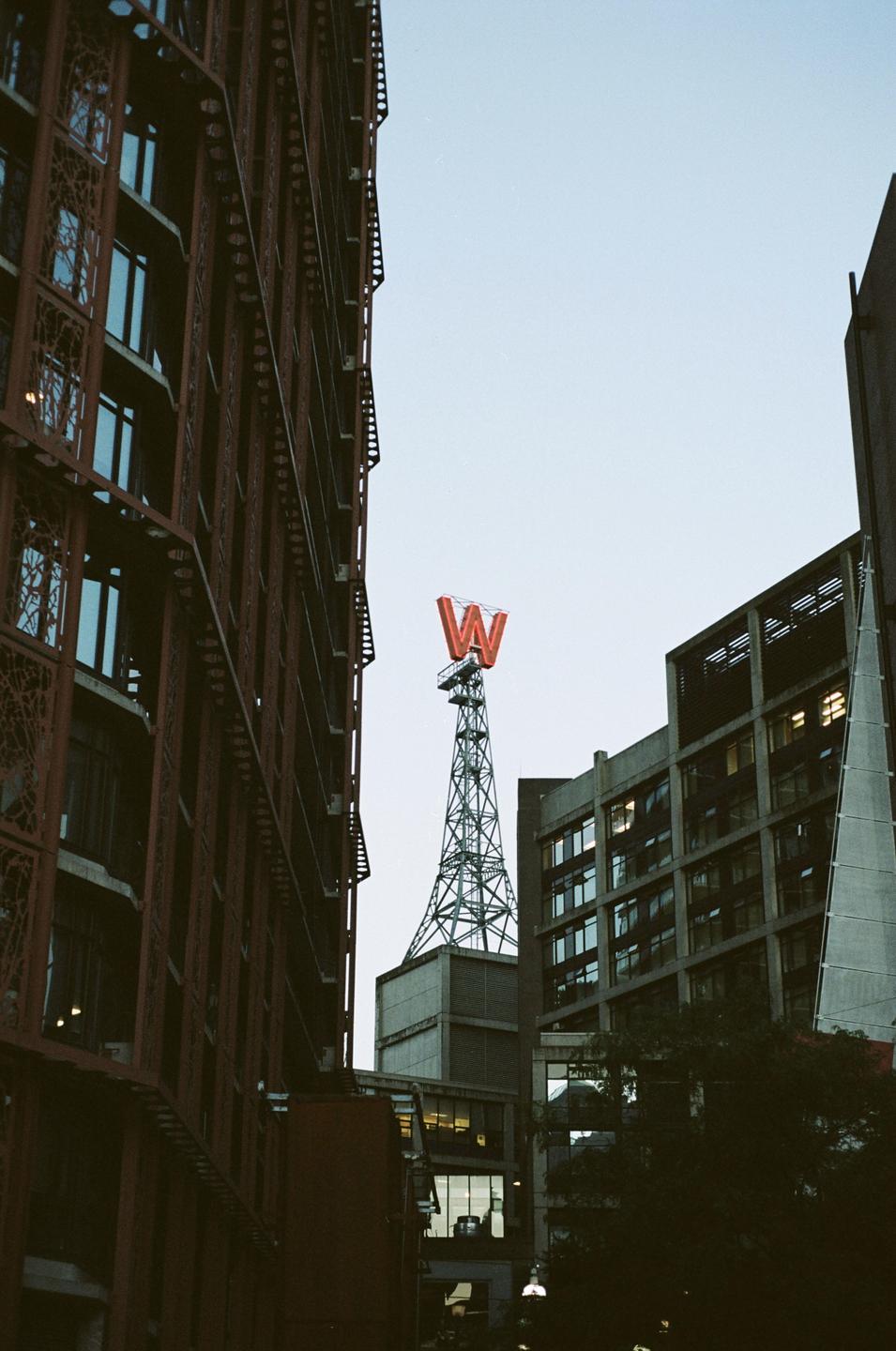 A red letter W sits atop a metal tower surrounded by buildings.