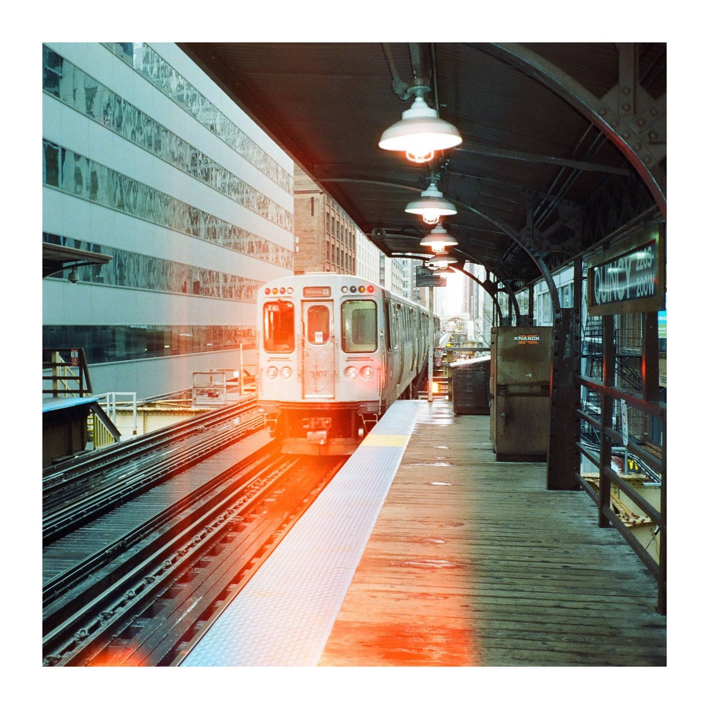 A train approaches a station platform with light leaks visible on the tracks and platform.