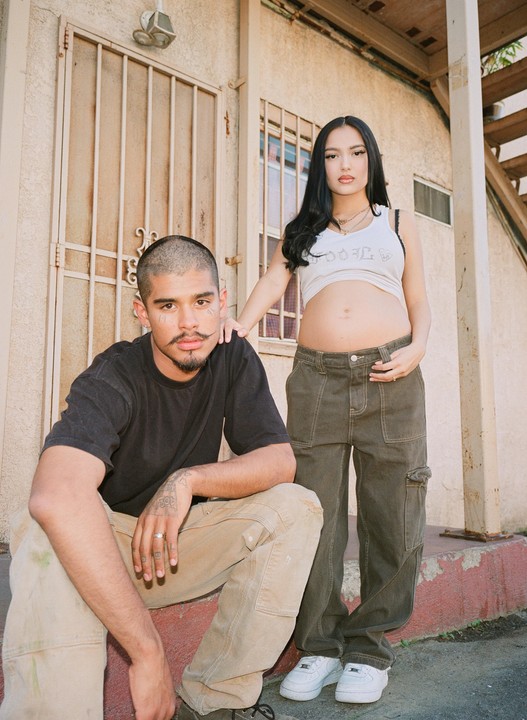 A man with a mustache and a pregnant woman pose for a portrait in front of a building.
