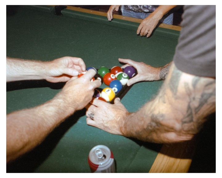 Three people arrange billiard balls on a pool table.