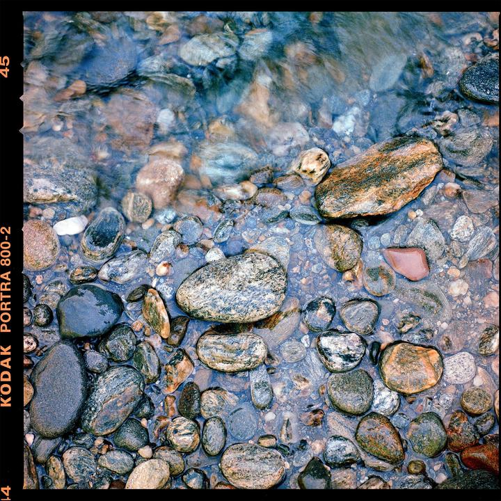 A collection of smooth, colorful stones are visible through clear, shallow water.