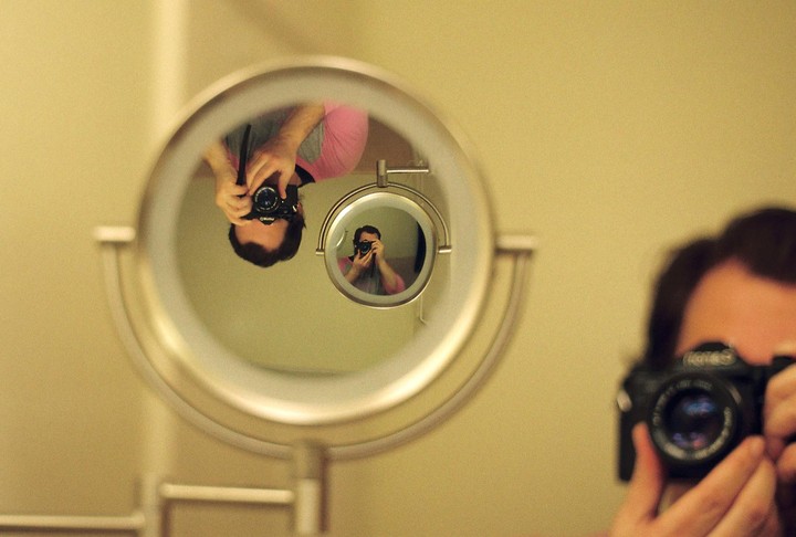 A man takes a self-portrait in a mirror, which reflects another mirror showing a smaller reflection of the man.