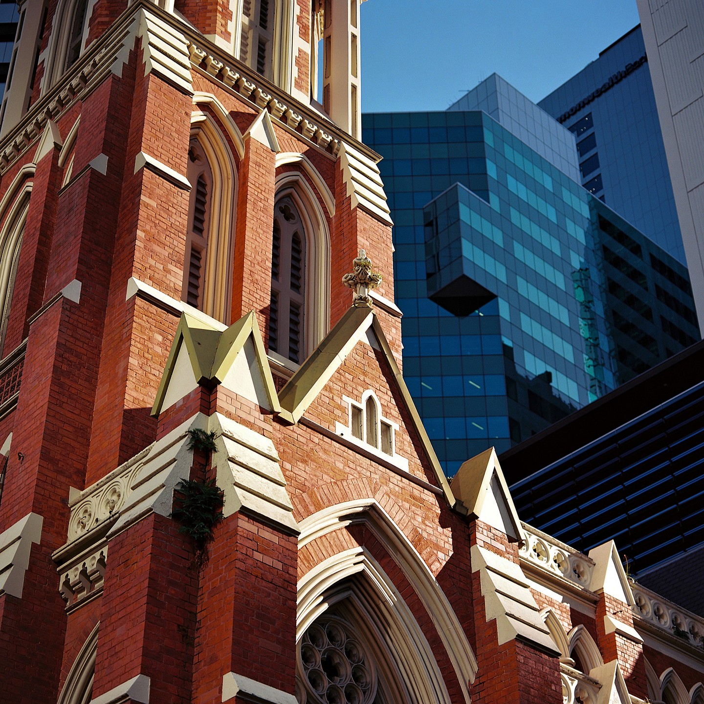 A red brick church with gothic architecture stands next to modern glass buildings under a clear sky.