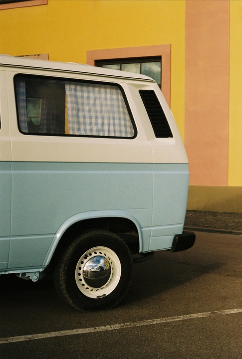 A light blue and white van is parked next to a building with yellow and peach walls.