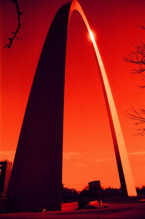 The Gateway Arch is visible against a red sky with the sun shining through its apex.