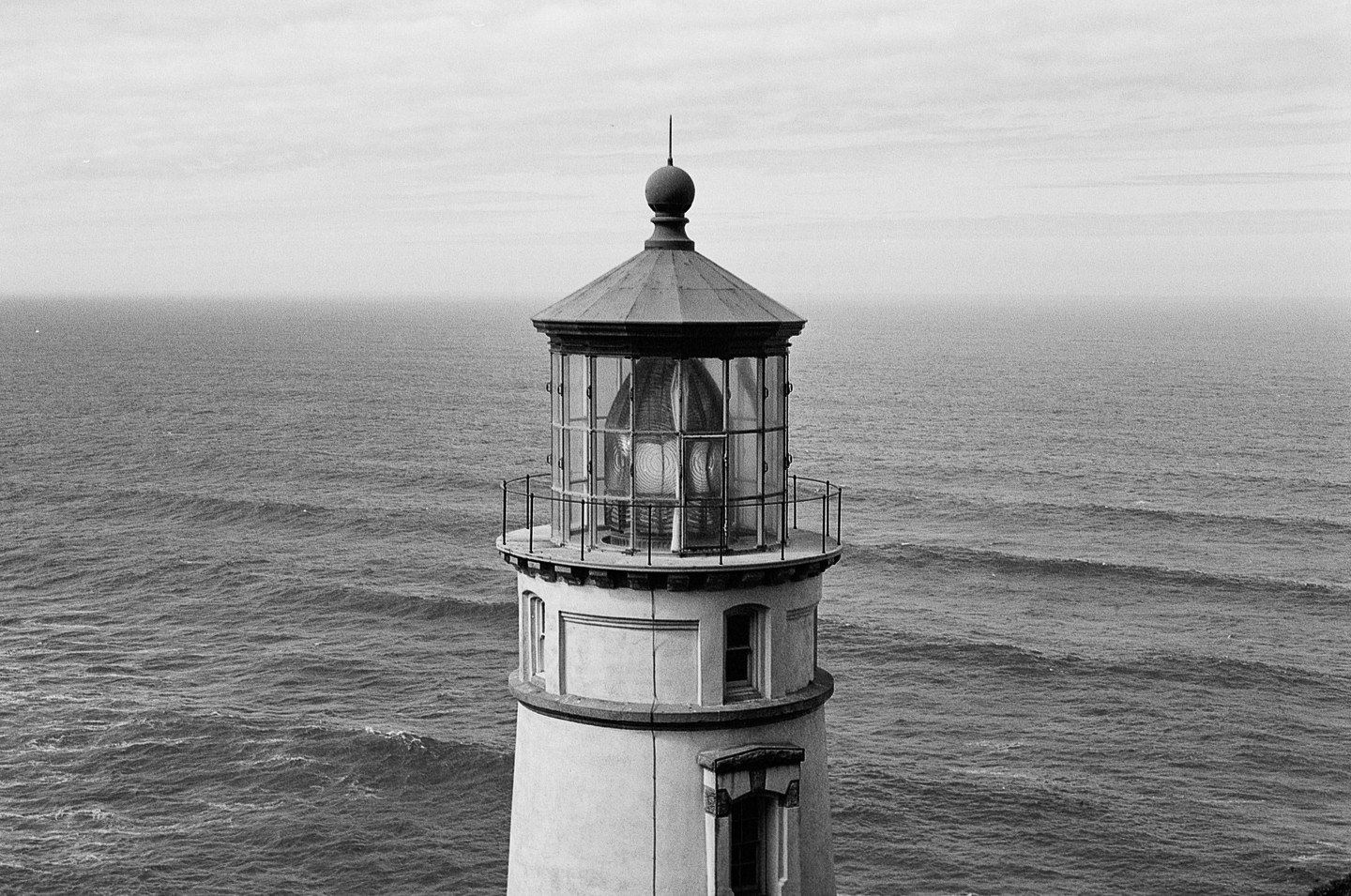 A lighthouse stands tall against a vast ocean under a cloudy sky.