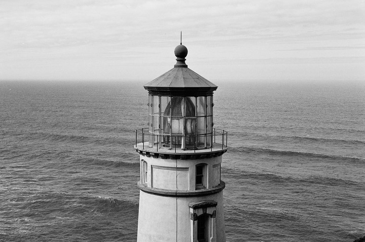 A lighthouse stands tall against a vast ocean under a cloudy sky.