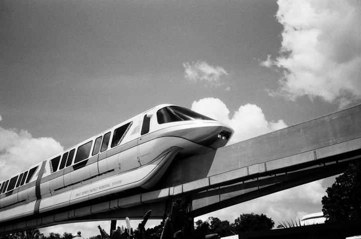 A monorail train travels on an elevated track against a cloudy sky.