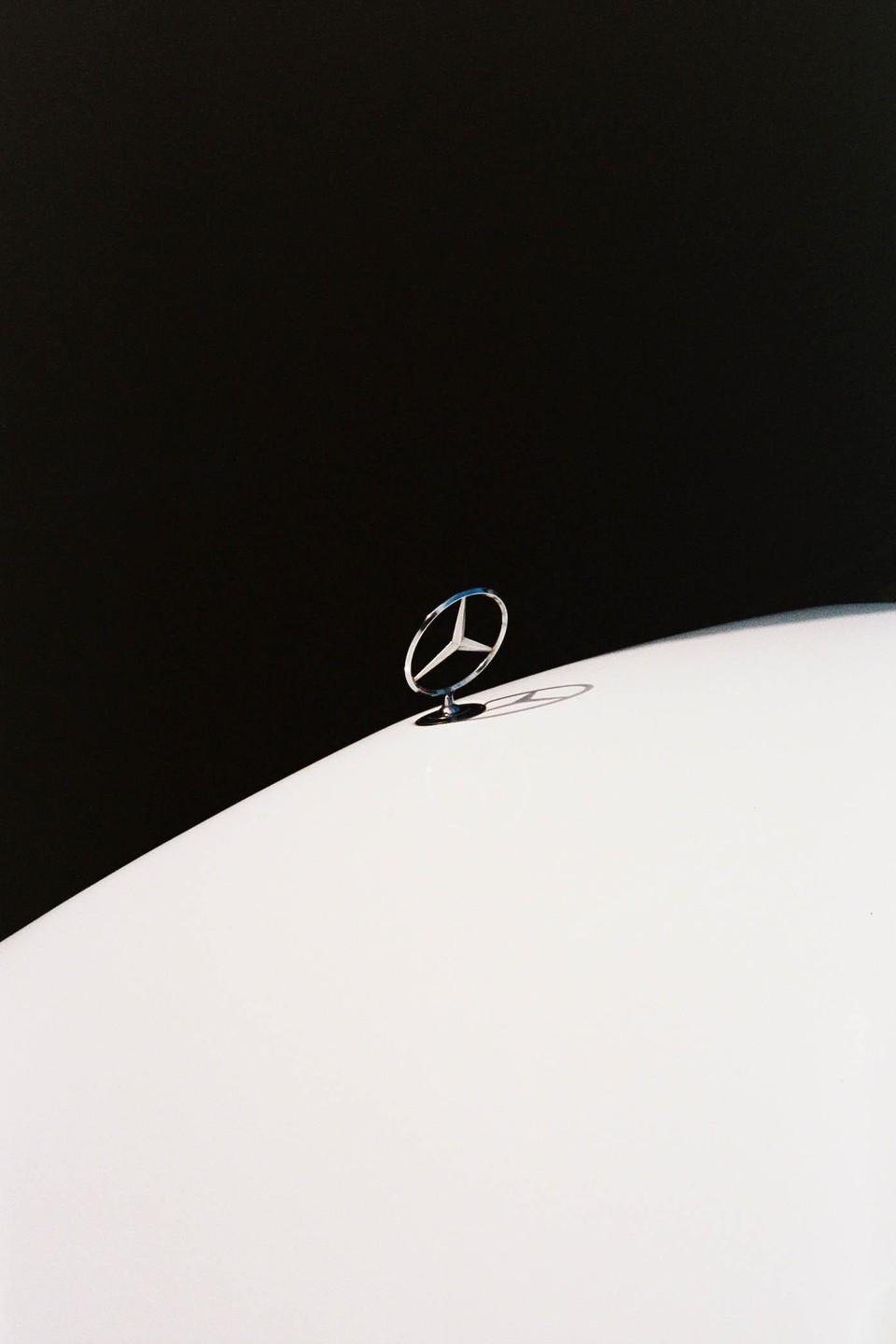 A Mercedes-Benz hood ornament is visible against a stark black background and a white car body.