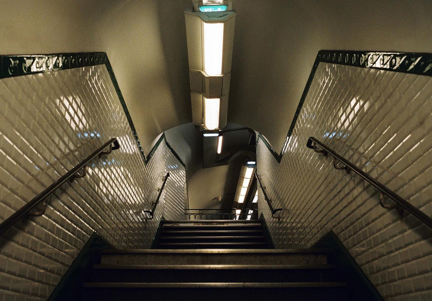 A long staircase with white tiled walls and handrails descends into a subway station.