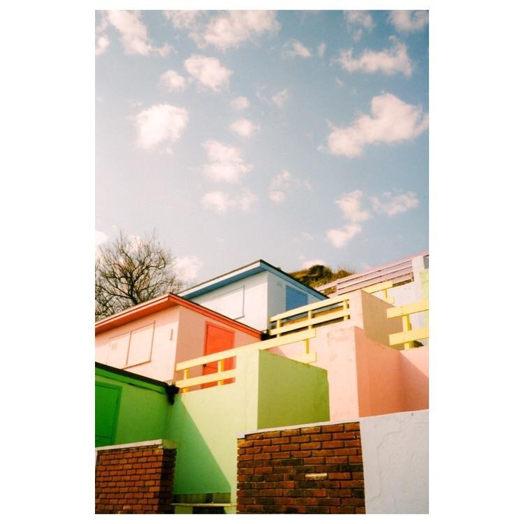 A collection of colorful beach huts are built into a hillside under a blue sky with white clouds.