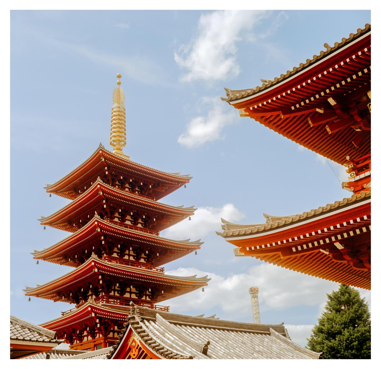 A red pagoda with a golden spire stands against a blue sky with white clouds, with another red roof visible on the right.