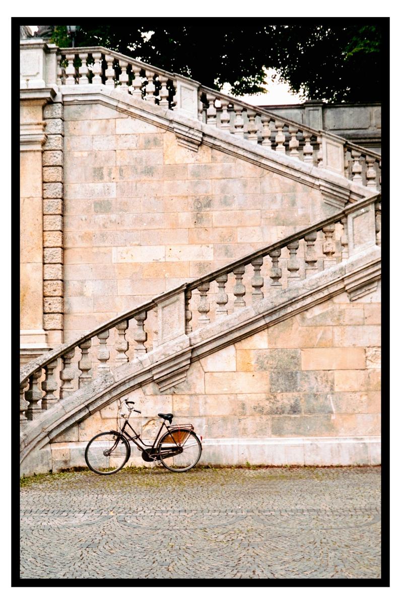 A bicycle is parked at the base of a grand stone staircase with a balustrade.
