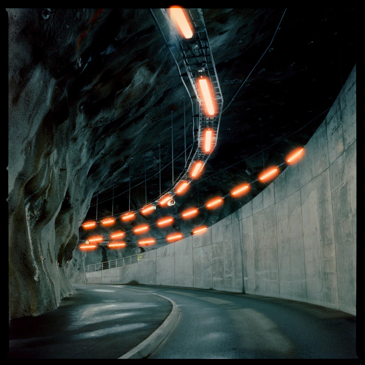 A curved road inside a tunnel is illuminated by a string of orange lights.