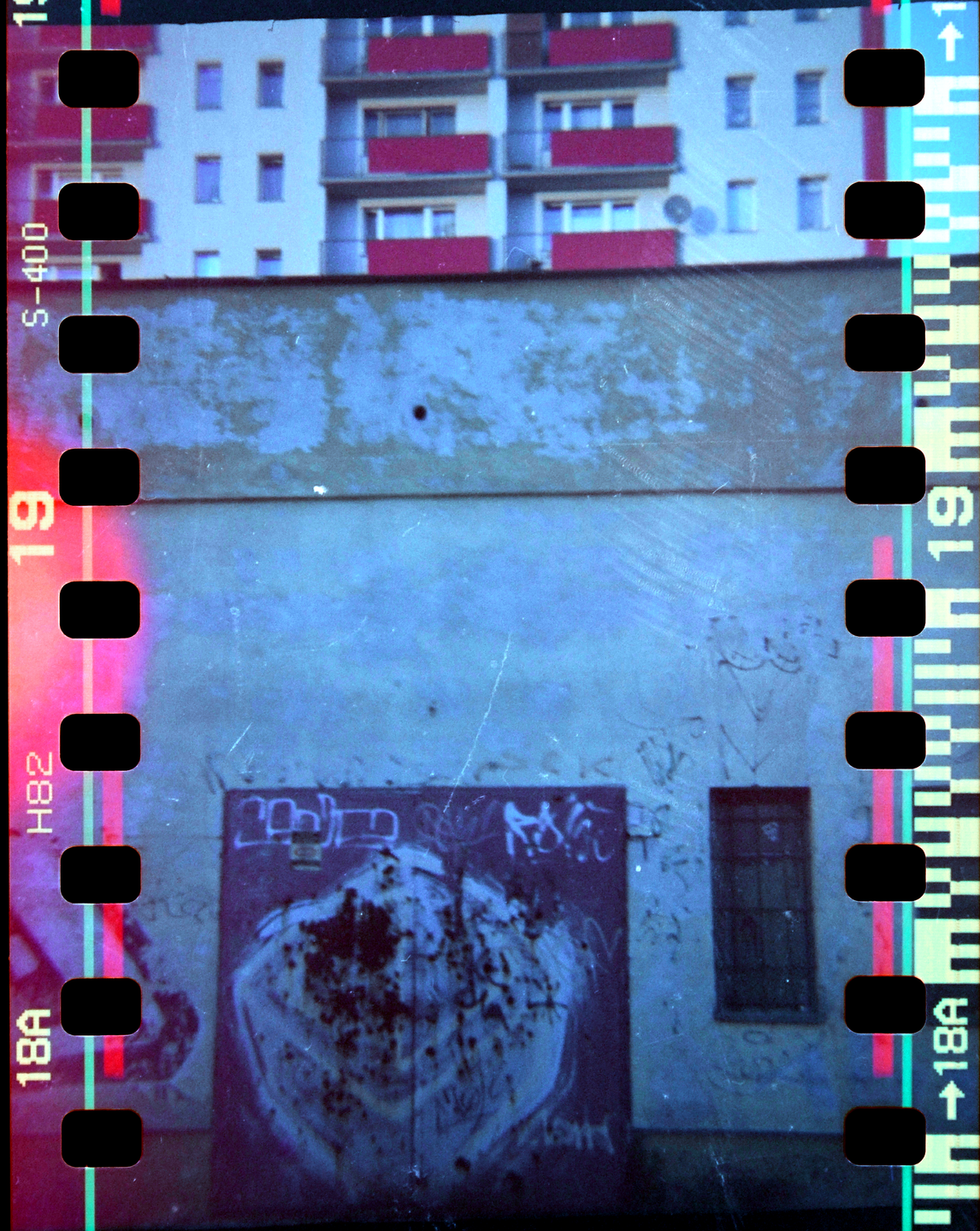 A building with red balconies is visible above a wall with graffiti and a window.