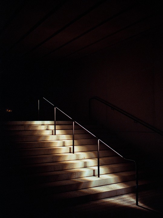 Light illuminates a concrete staircase with metal railings in a dark setting.