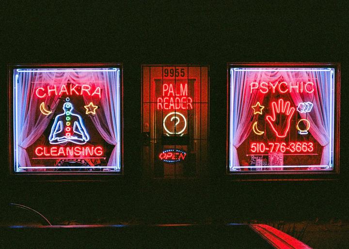 Three neon signs for a psychic and palm reader glow in the dark.