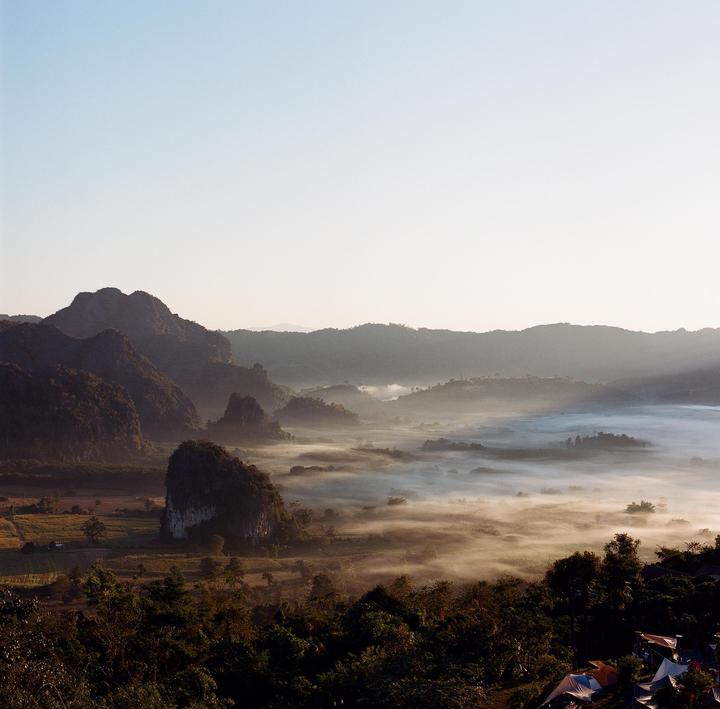 A wide landscape shows a valley filled with fog and surrounded by mountains under a clear sky.