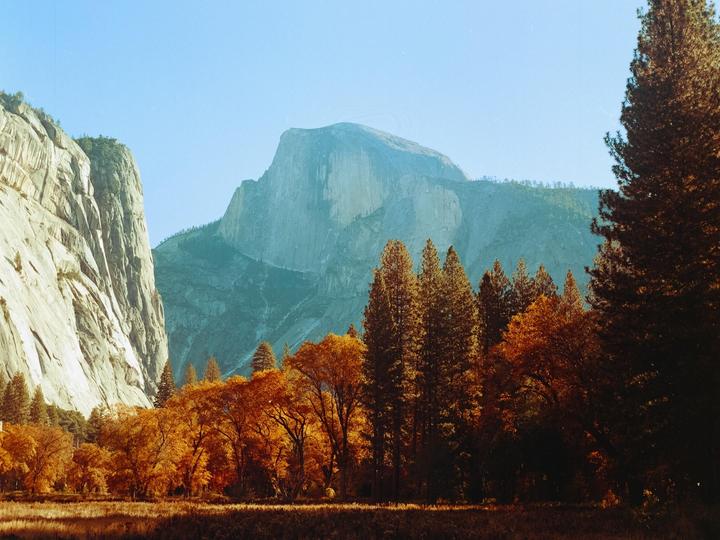 A valley with autumn trees and tall mountains under a clear sky.