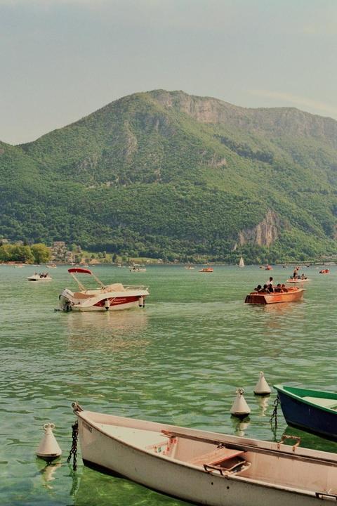 Several boats are on a lake with a large, tree-covered mountain in the background.