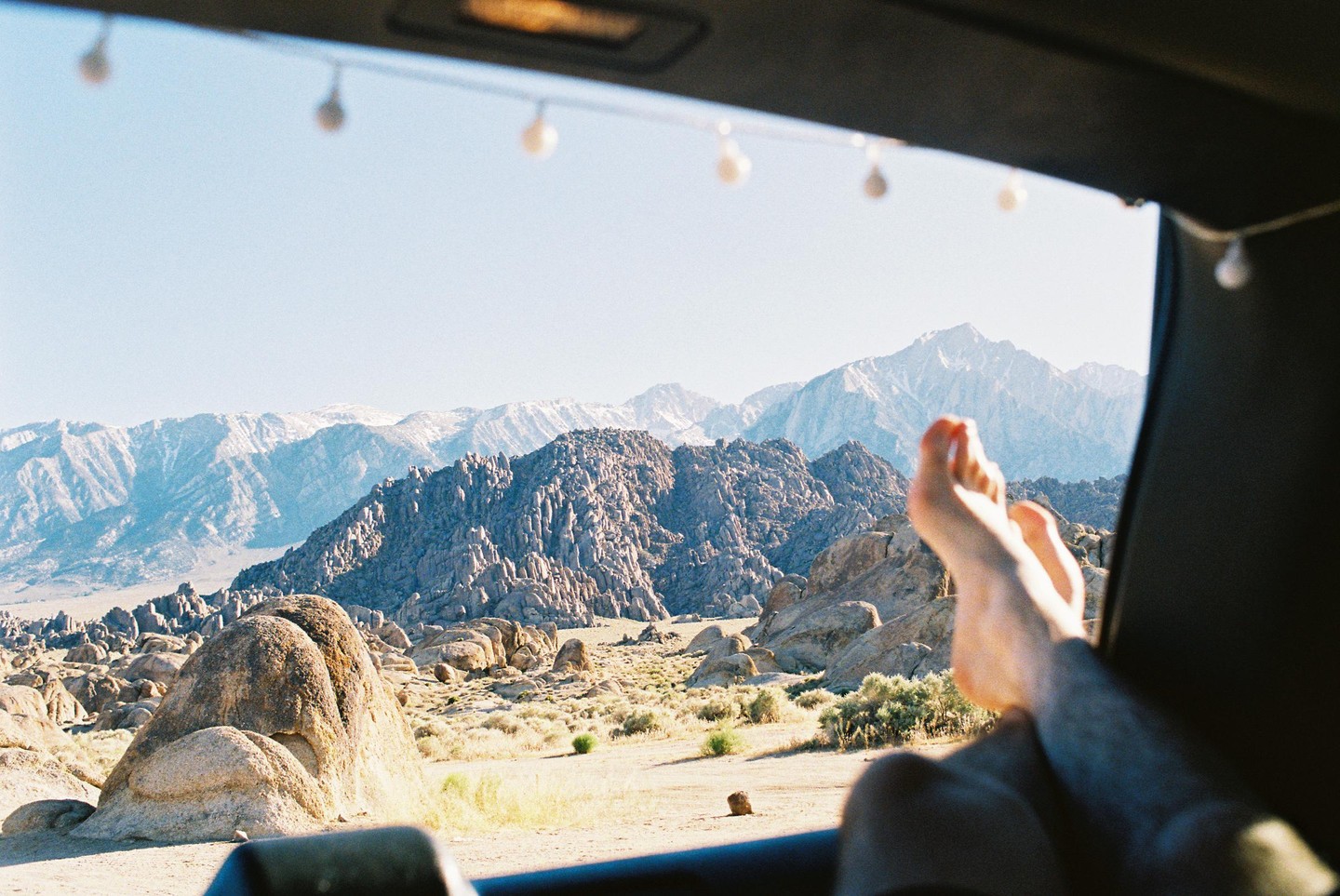 A person's feet are visible in the foreground, with a desert landscape and mountains in the background.