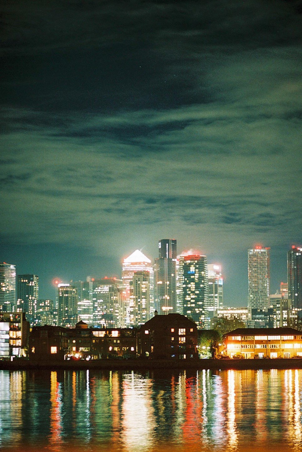 The London skyline is illuminated at night with reflections visible in the water.