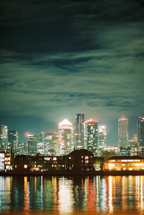 The London skyline is illuminated at night with reflections visible in the water.