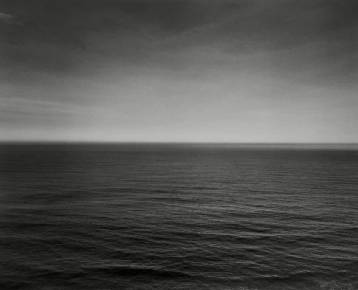 The vast Pacific Ocean stretches to the horizon under a cloudy sky.