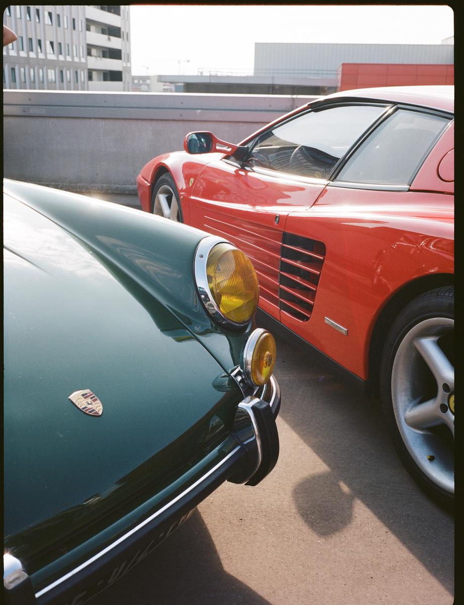 A green vintage car is parked next to a red sports car on a rooftop.