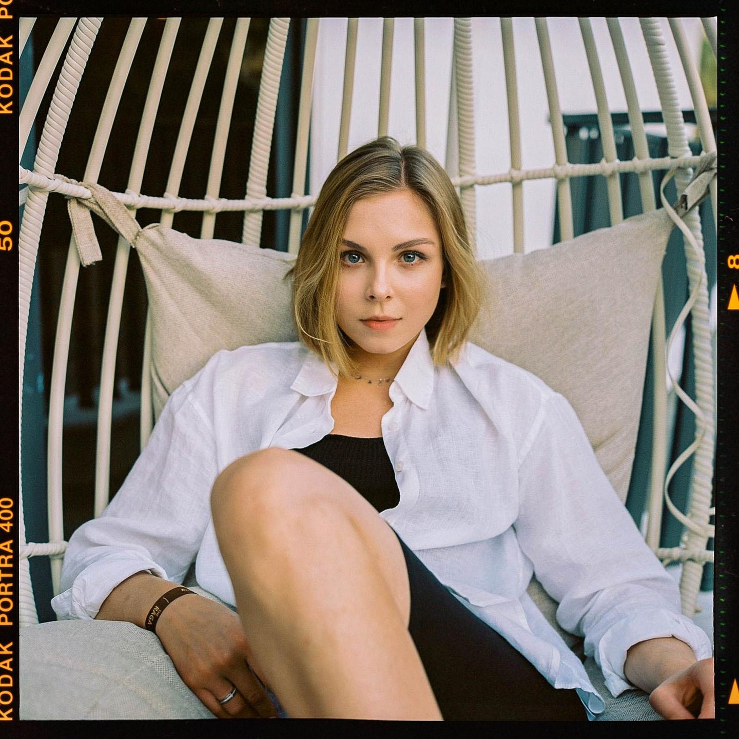 A woman with short hair and a white shirt sits in a hanging chair.