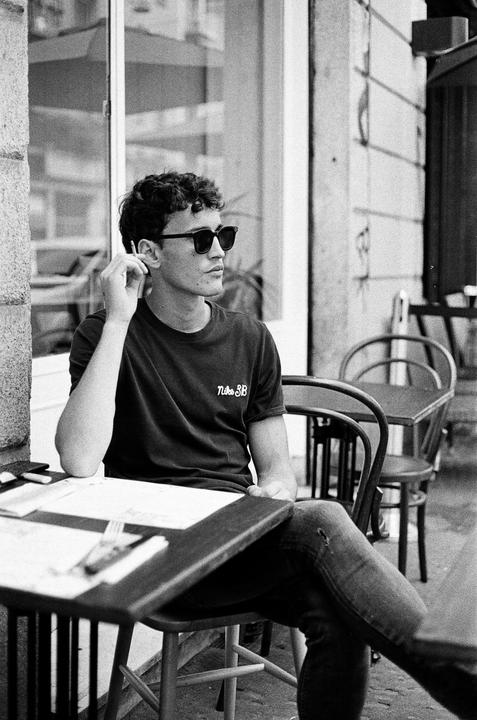 A man wearing sunglasses and a t-shirt sits at a table on a patio.
