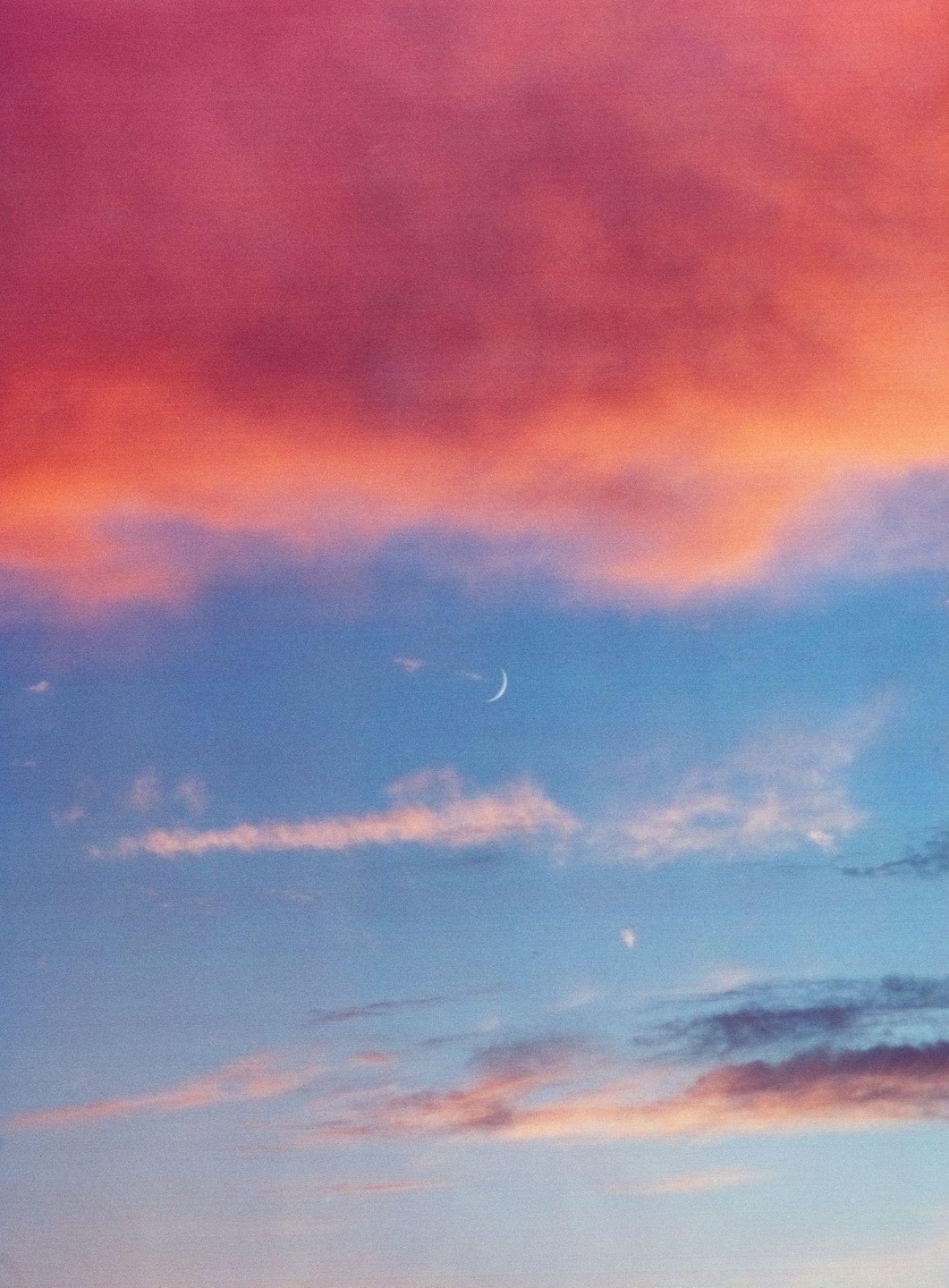 A crescent moon is visible in a colorful sky with clouds at sunset.