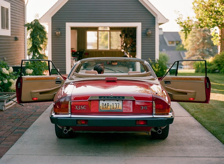 A red convertible car with its doors open is parked on a driveway in front of a garage.