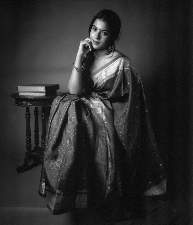 A woman in a sari sits next to a small table with books.