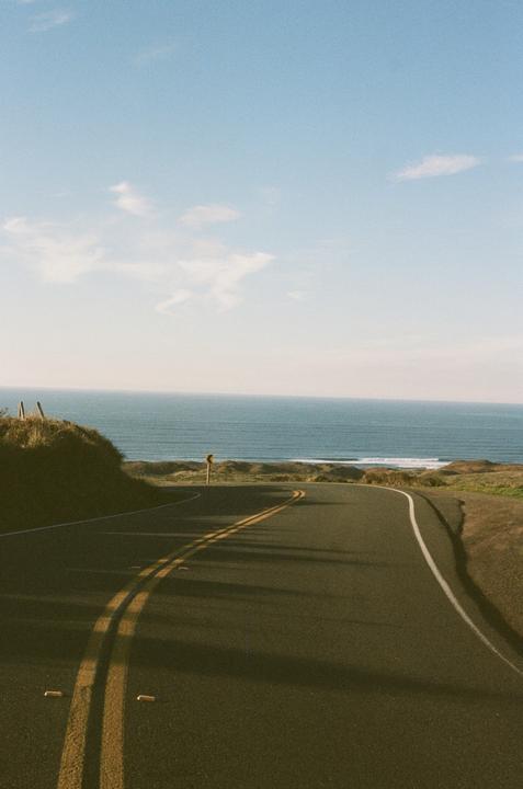 A winding road leads towards the ocean under a clear sky.