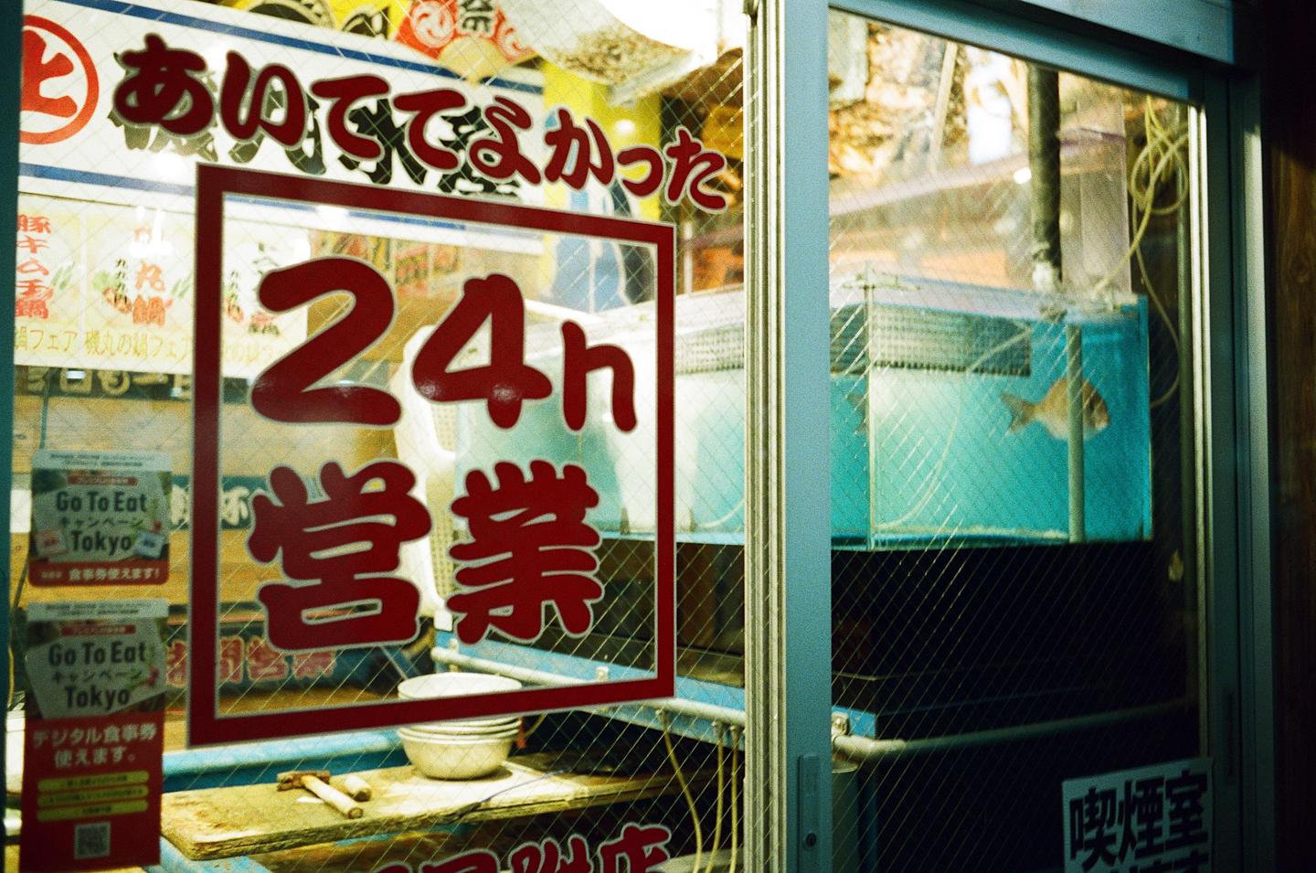 A fish swims in a tank next to a window with a "24h" sign.