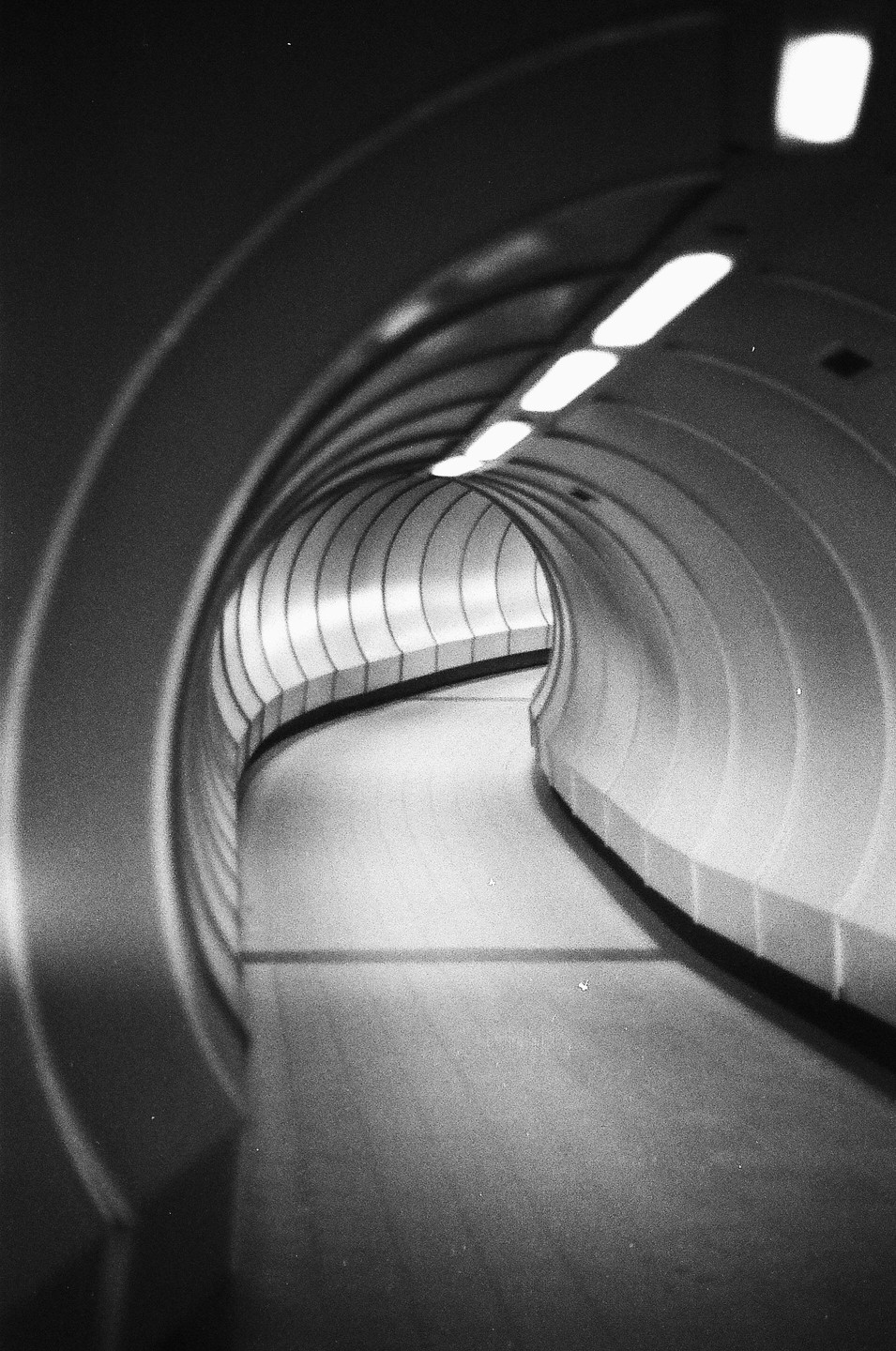 A black and white photograph shows a long, curving tunnel with lights on the ceiling.