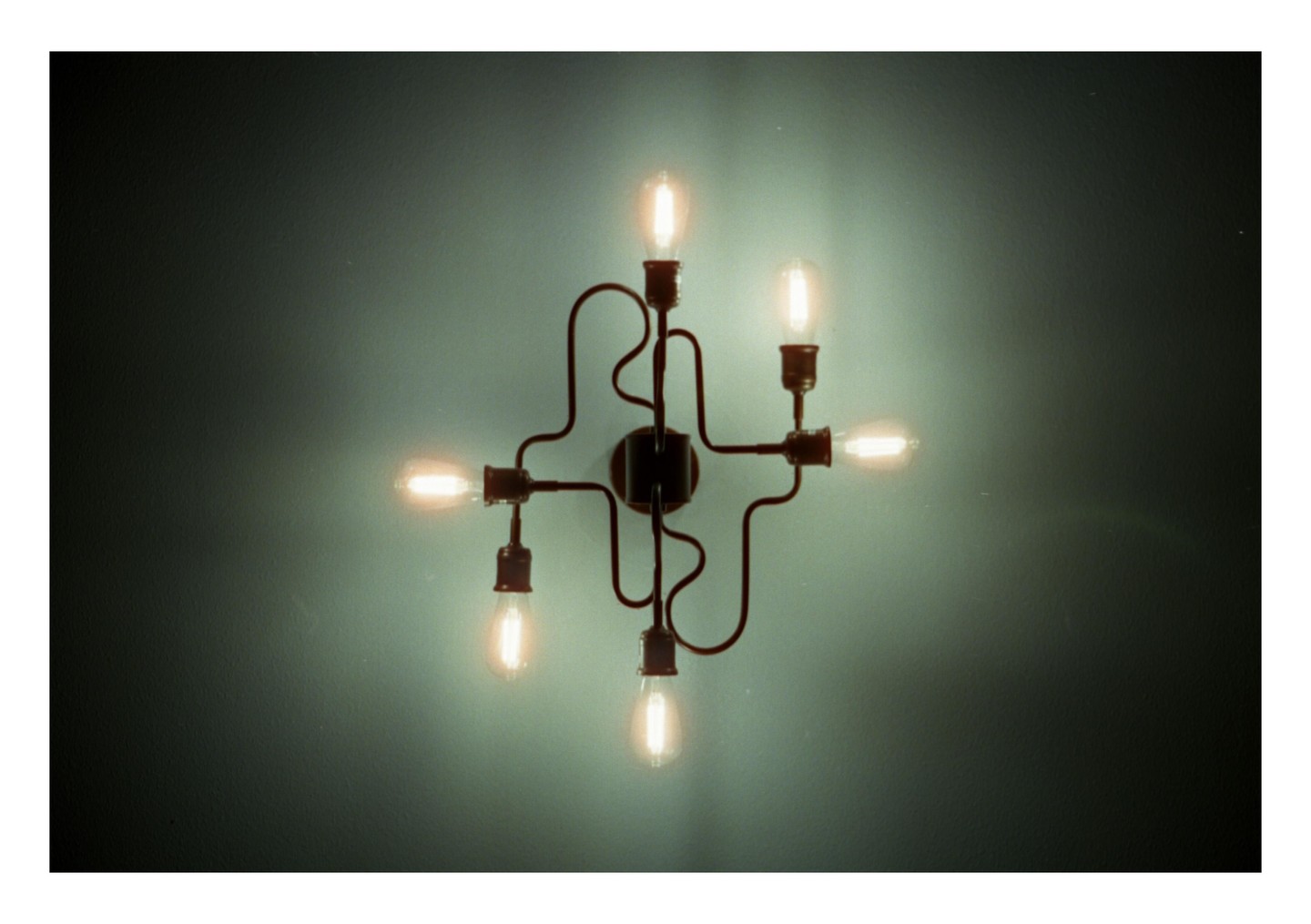 A wall-mounted light fixture with six exposed bulbs illuminates a textured wall.