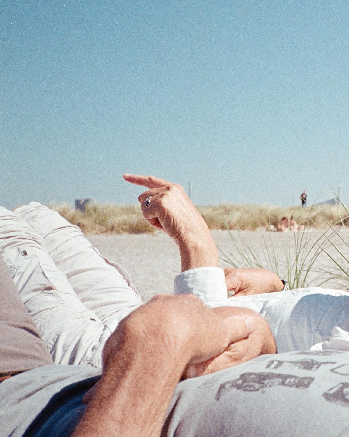 A person points towards the horizon from a beach with tall grass.