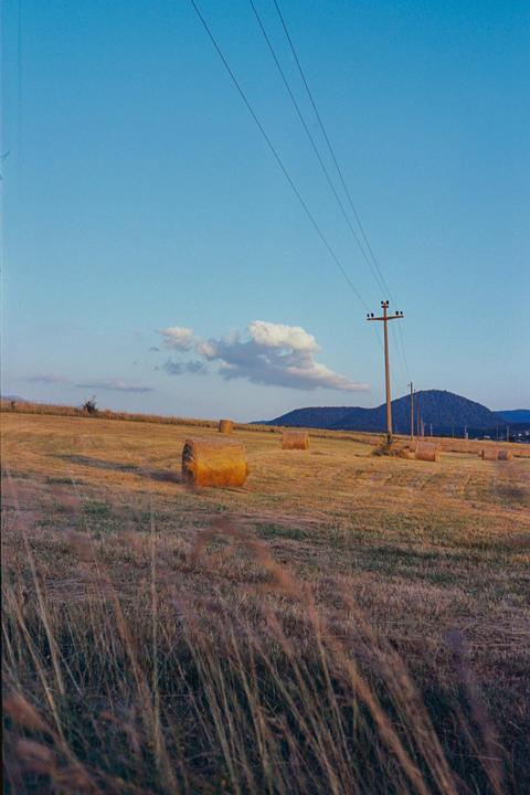 A field with several hay bales and a utility pole under a blue sky with a few clouds.