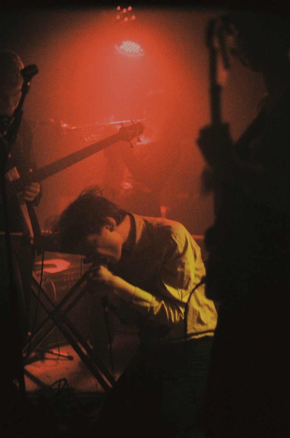A man sings into a microphone on a stage lit with red light.