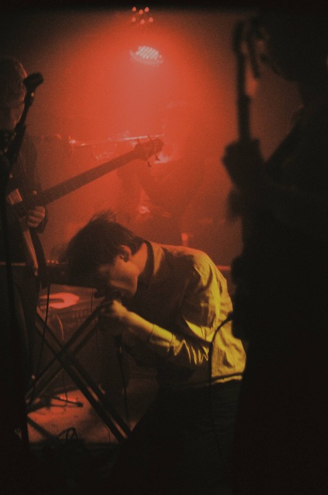 A man sings into a microphone on a stage lit with red light.